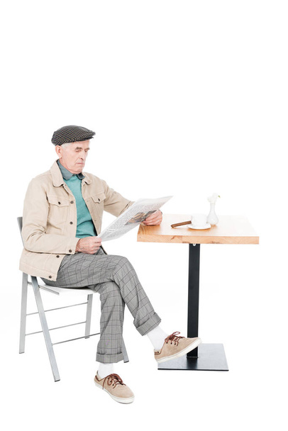 retired man reading newspaper while sitting on chair with crossed legs isolated on white - Zdjęcie, obraz