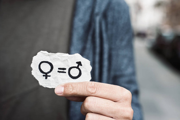 Close-up van een Kaukasische persoon op straat met een stuk papier met de voorstelling van de gendergelijkheid getrokken in het - Foto, afbeelding