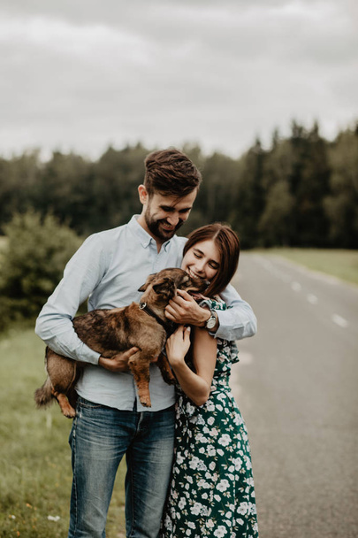 Retrato de pareja joven enamorada abrazándose con el perro en el campo verde
 - Foto, imagen