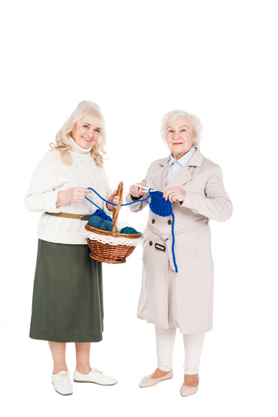 cheerful retired woman knitting near friend holding basket isolated on white - Zdjęcie, obraz
