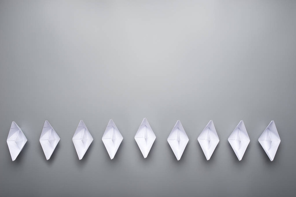 Vista dall'alto di nove barche origami fatte di carta nella parte inferiore dell'immagine su sfondo grigio con abbondanza di spazio per la copia
. - Foto, immagini