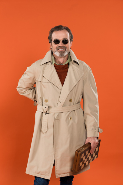 cheerful senior man in sunglasses standing with chess board isolated on orange - Φωτογραφία, εικόνα