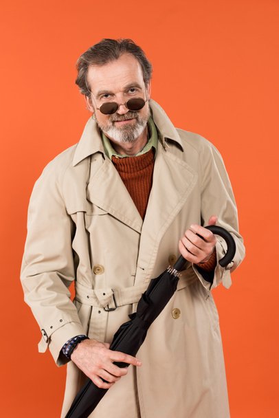 cheerful senior man in sunglasses holding umbrella isolated on orange - Foto, Imagen