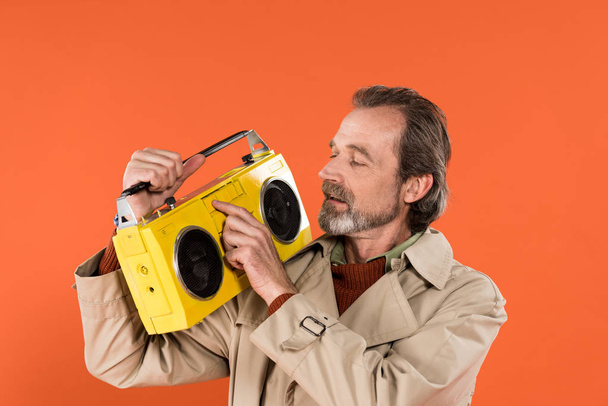 cheerful retired man touching yellow boombox isolated on orange - Fotografie, Obrázek