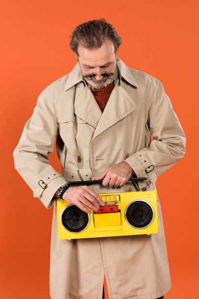 alegre aposentado homem pressionando botão amarelo boombox isolado em laranja
 - Foto, Imagem
