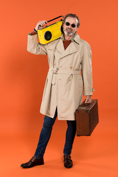 vrolijk gepensioneerde man met gele boombox en werkmap in handen op een oranje achtergrond - Foto, afbeelding