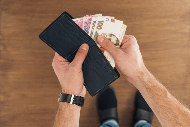 top view of man puting hryvnyas banknotes in wallet on wooden background - Foto, Bild