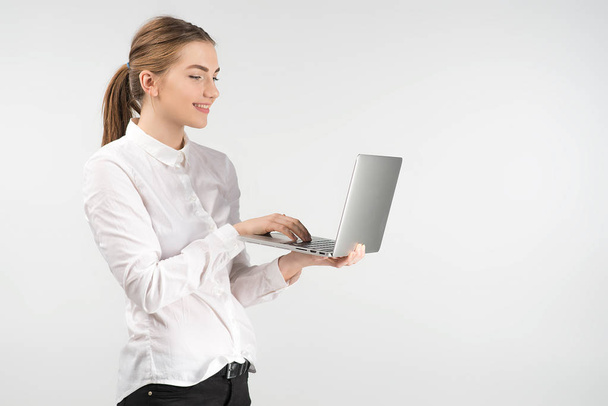 Smiling business woman in white shirt  holding laptop and working while standing - Foto, Imagen