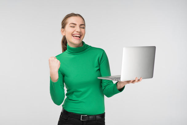 Happy girl looking at laptop with laughing surprised expression . Holds device and fist up. - Concept image - Foto, afbeelding