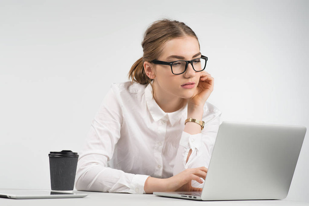 Femme d'affaires intelligente assise et travaillant soigneusement derrière un ordinateur portable avec une tasse de café et ipad sur la table
 - Photo, image