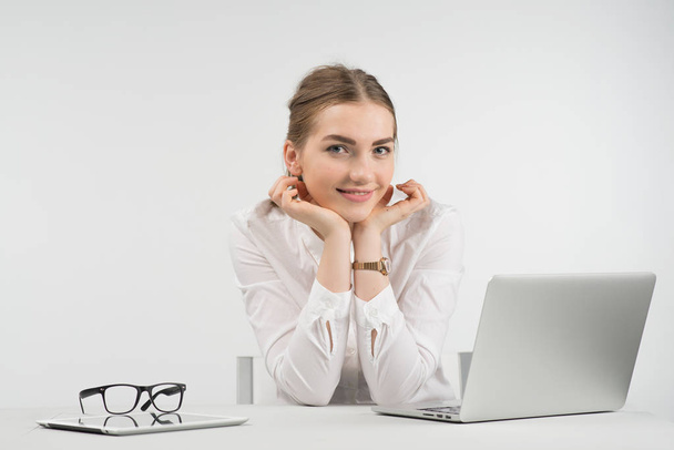Lachende mooie vrouw zitten naast een laptop en de camera haar hoofd zetten door het haar te kijken armen - Foto, afbeelding