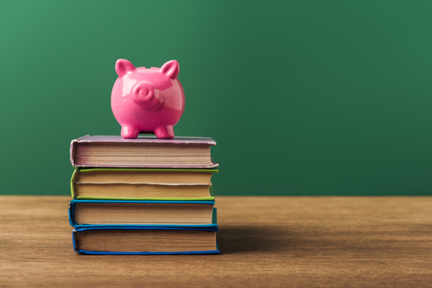pink piggy bank on books, wooden table and green background - Foto, afbeelding