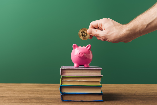 man puting coin in pink piggy bank on books with green background - Photo, Image