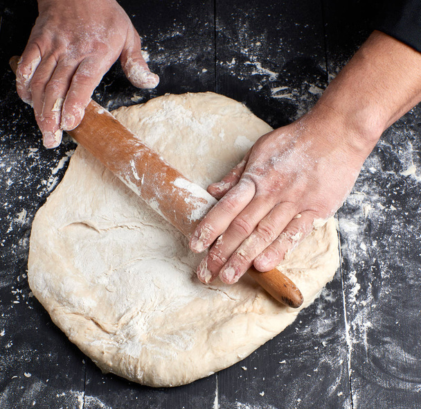 шеф-кухар в чорній туніці робить тісто для круглої піци, вид зверху
 - Фото, зображення
