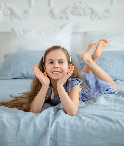 Happy little girl in a bright room is lying on the bed. Good mood on a holiday. - Foto, afbeelding