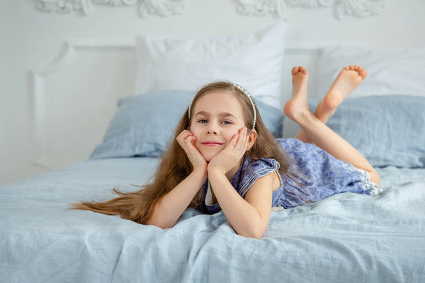 Happy little girl in a bright room is lying on the bed. Good mood on a holiday. - Foto, Bild