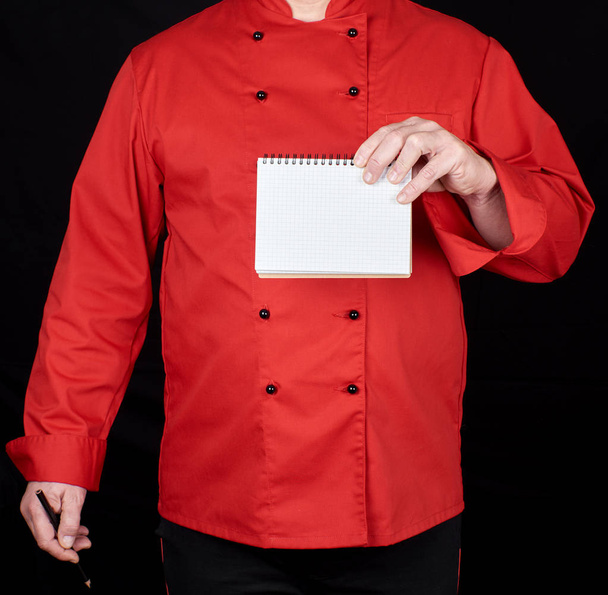 chef in red uniform  holding a blank paper notebook, black background, copy space - Фото, изображение