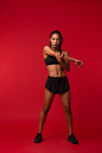 Image of a strong young african sports fitness woman posing isolated over red wall background make exercises. - Fotó, kép