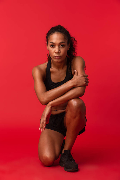 Image of a beautiful young african sports fitness woman posing isolated over red wall background. - Valokuva, kuva