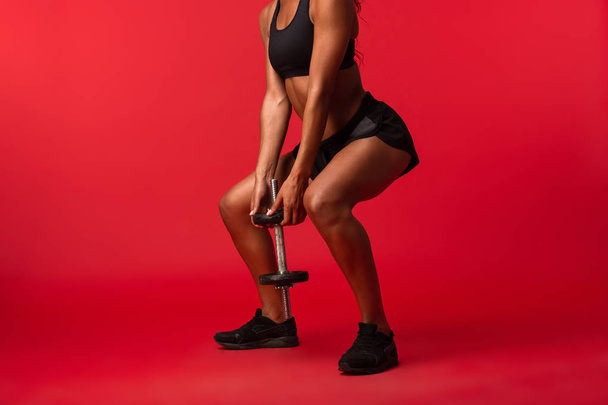 Image of skinny african american woman in black sportswear lifting dumbbell isolated over red background - Foto, Bild