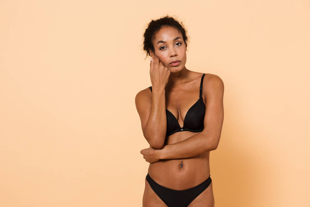 Image of american woman wearing black lingerie standing isolated over beige background - 写真・画像