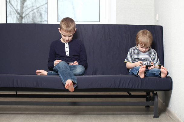 mother with two brothers blond boys on a blue sofa at home playing smartphones - Фото, зображення