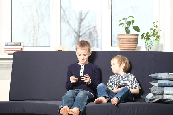 mother with two brothers blond boys on a blue sofa at home playing smartphones - Foto, imagen