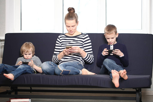 mère avec deux frères blonds garçons sur un canapé bleu à la maison jouer smartphones
 - Photo, image
