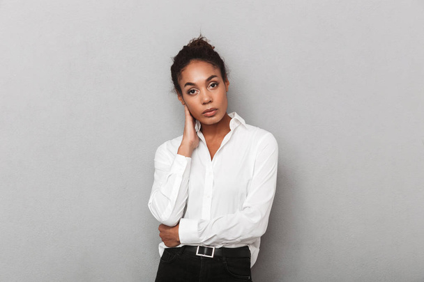 Attractive young african business woman wearing shirt standing isolated over gray background, looking at camera - Foto, afbeelding