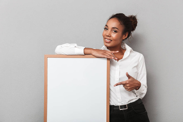 Smiling african business woman wearing a shirt standing isolated over gray background, presenting blank board - Фото, зображення