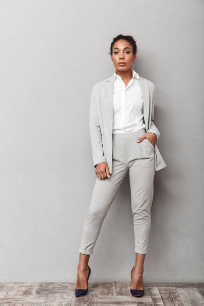 Full length portrait of a confident african business woman wearing suit standing over gray background, posing - Fotoğraf, Görsel