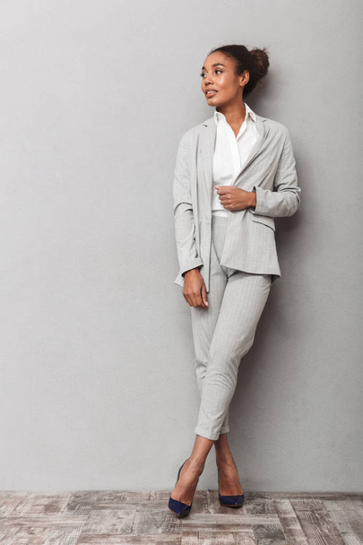 Full length portrait of a confident african business woman wearing suit standing over gray background, posing - Фото, изображение