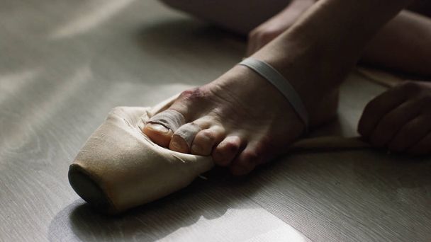Close-up of ballerinas feet. Ballerina preparing for training, and tying ribbon of pointe shoes sitting on floor in bright sunlight - Foto, Bild