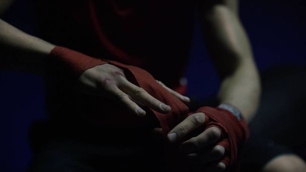 Boksörler el Close-up. Yakın çekim boksör bağları ile kırmızı kurdele eğitim için hazırlanıyor karanlık soyunma odasında el yaralı - Fotoğraf, Görsel