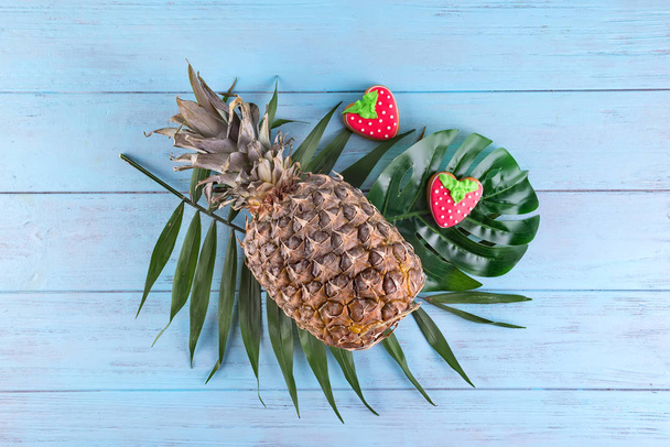 Tropical pineapple with homemade glazed cookies served on palm leaves on blue wooden background. Healthy food, flat lay - Photo, Image