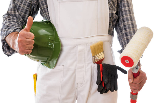 House painter worker in white work overalls with thumb up, holds in his hand the roller to paint. Equipped with protective gloves. Isolated on white background. Construction industry. - Foto, Imagen
