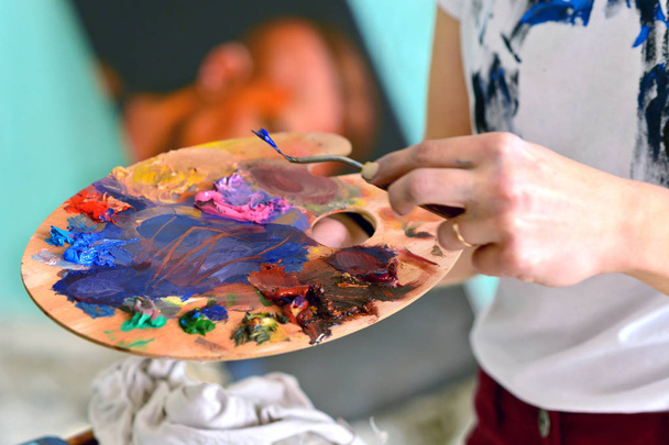 Palette with colors in the hand of the girl. cleans off unnecessary paint. The concept of fine arts - Zdjęcie, obraz