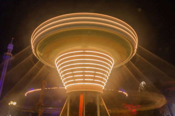 Een wazig kleurrijke keten carrousel in beweging op het pretpark, nacht verlichting. Het effect van de bokeh en lange blootstelling - Foto, afbeelding
