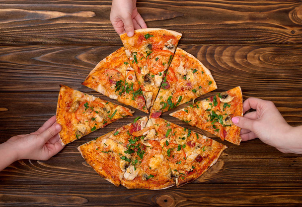 Hands taking pizza slices from wooden background. - Fotografie, Obrázek