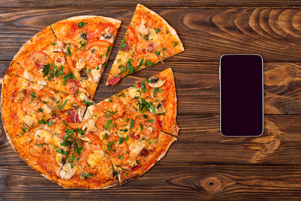 Fresh baked pizza and smartphone on wooden table with copy space. Food delivery  - Foto, Imagen