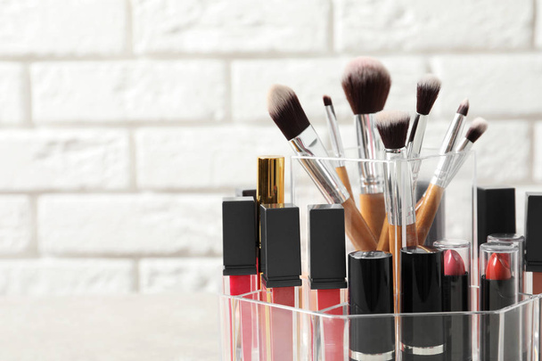 Lipstick holder with different makeup products on table against brick wall, closeup. Space for text - Photo, image