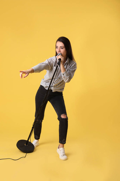 Young woman wearing casual clothes singing in microphone on color background - Photo, Image