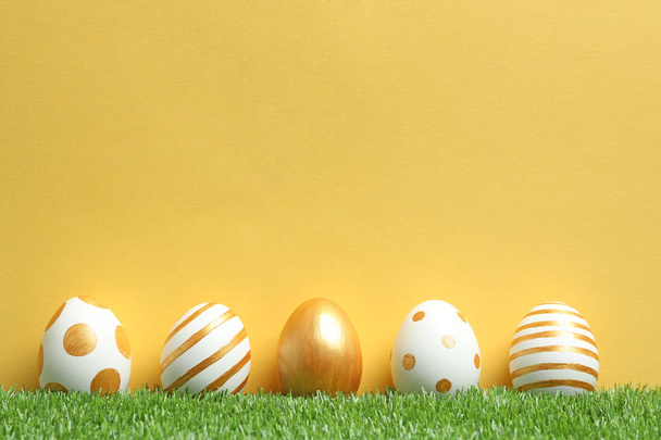 Line of traditional Easter eggs decorated with golden paint on green lawn against color background, space for text - Photo, image