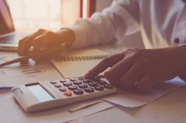 Ręką człowieka za pomocą Kalkulator finansowy z pisania sprawiają, Uwaga i analizowanie danych finansowych na biurku w domu  - Zdjęcie, obraz