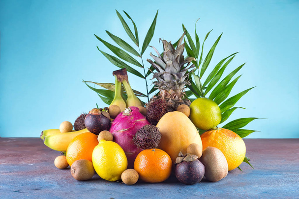 Vegyes trópusi gyümölcsök, narancs, Ananas vagy ananász, lime, mango, sárkány gyümölcs, narancs, banán, rambutan és lichi a kék háttér. Másolja a hely - Fotó, kép