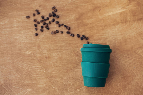 Zero waste concept, flat lay. Stylish reusable eco coffee cup on wooden background with roasted coffee beans. Ban single use plastic. Sustainable lifestyle. Natural bamboo cup - Photo, Image
