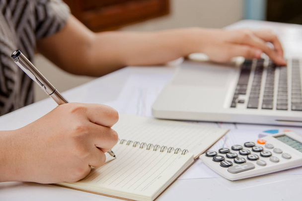 γυναίκα το χέρι γραφής κάνουν σημείωση και χρησιμοποιούν φορητό υπολογιστή στο χαρτί γραφήματος δεδομένων με κάνει οικονομικών στο γραφείο. - Φωτογραφία, εικόνα