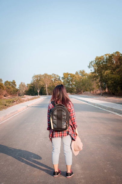 Travel concept. Traveling woman with backpack walking on asphalt road countryside - Фото, изображение