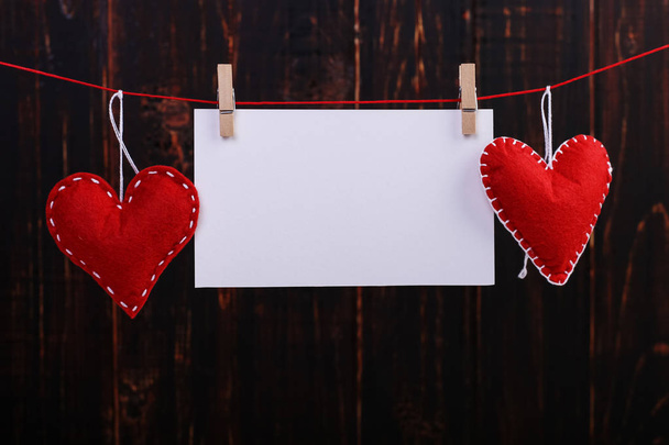 Handmade red felt hearts and white paper hanging on rope with clothespins. Concept, banner, copy space, form. - Photo, image