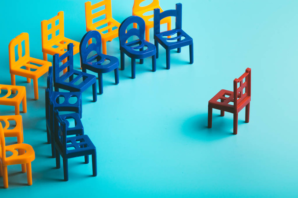 on a blue background with plenty of chairs, plastic, yellow and blue stand in a semicircle in two rows and one red separately at the center, toy chairs - Photo, Image